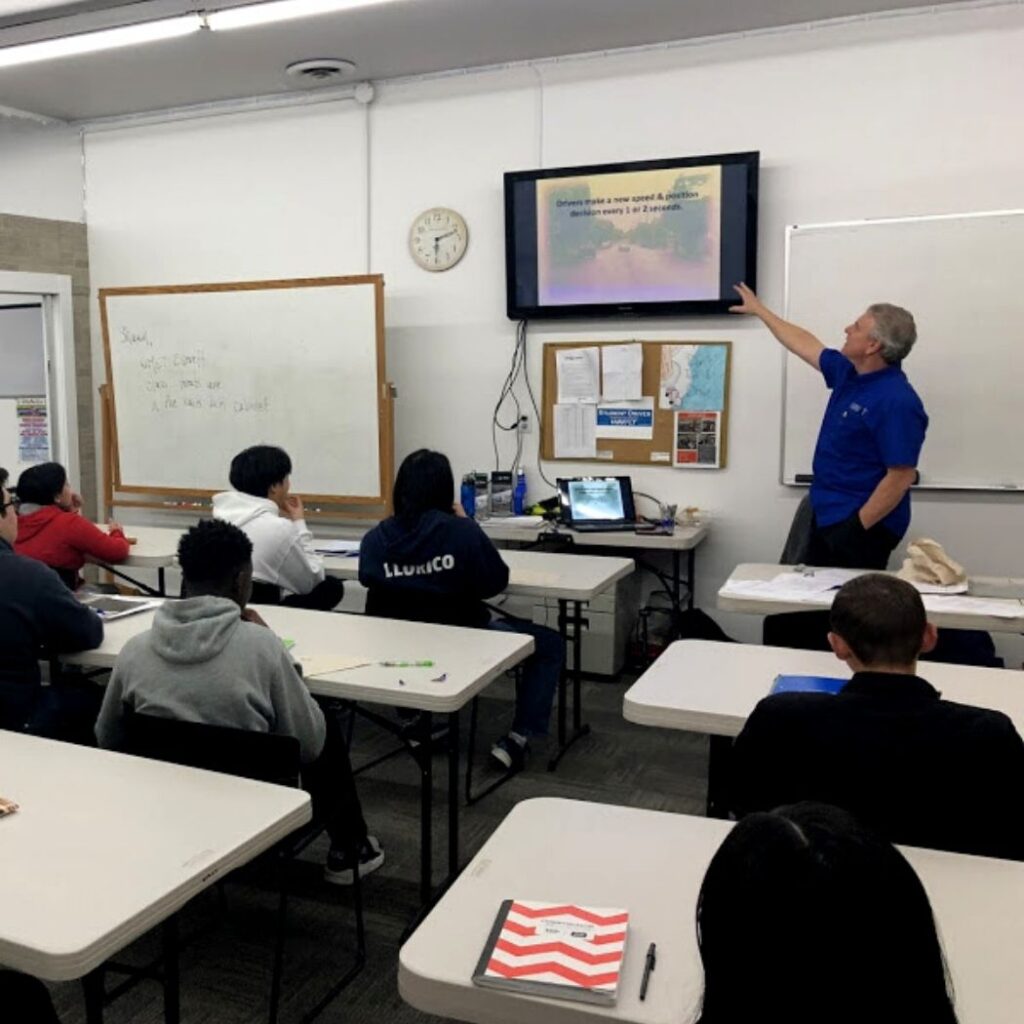 drivers education instructor pointing to the board with students taking notes